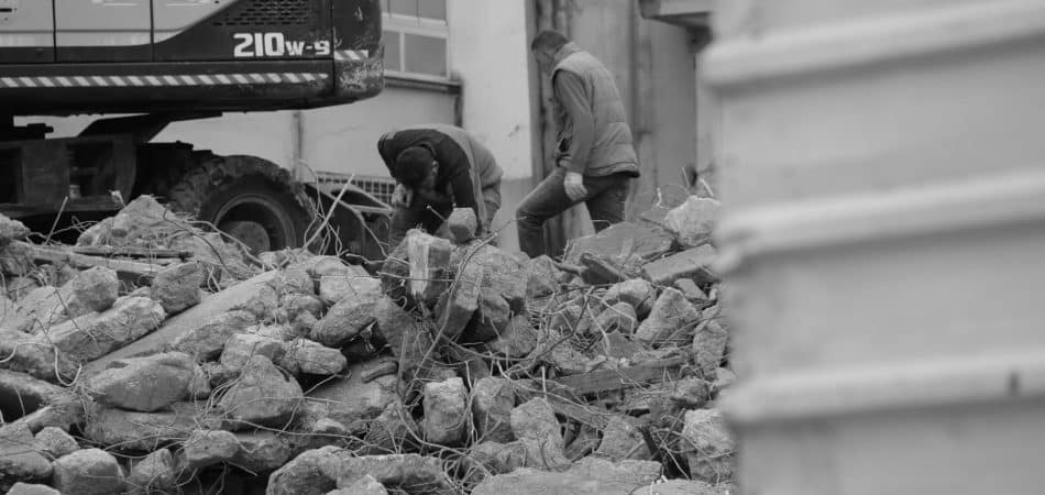 Black and white photo of workers and heavy machinery at a demolished construction site.